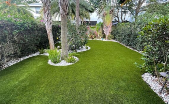 A lush artificial grass backyard with modern landscaping and flower beds.